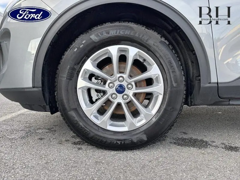 Gros plan sur la roue avant gauche d'un Ford Kuga gris Solar Métallisée avec jante alu et logo Ford central.