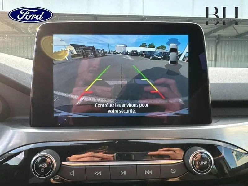 Écran tactile intérieur du Ford Kuga 2023 montrant la caméra de recul avec guidage coloré sur parking extérieur.