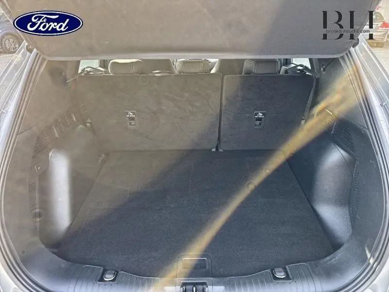 Coffre spacieux du Ford Kuga 2023 gris Solar Métallisé, vue arrière avec banquette arrière relevée et tapis noir.