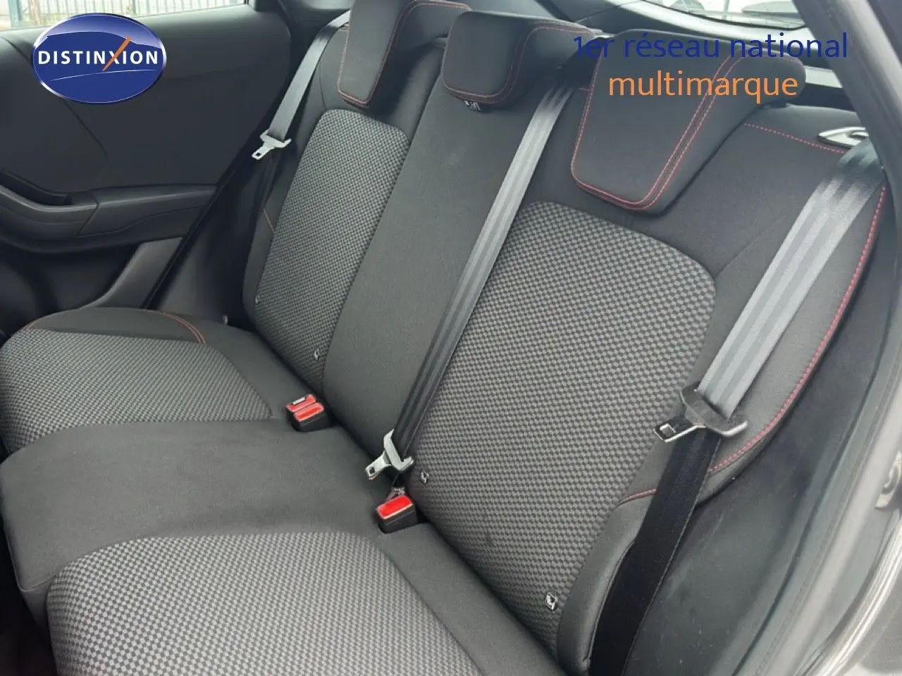 Vue intérieure sur les sièges arrière en tissu noir à motifs gris avec surpiqûres rouges, porte ouverte côté droit.
