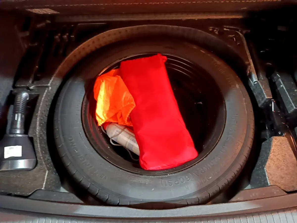 Gros plan sur la roue de secours dans le coffre d'un Volkswagen Tiguan 2021, avec trousse de secours rouge et gilet orange.