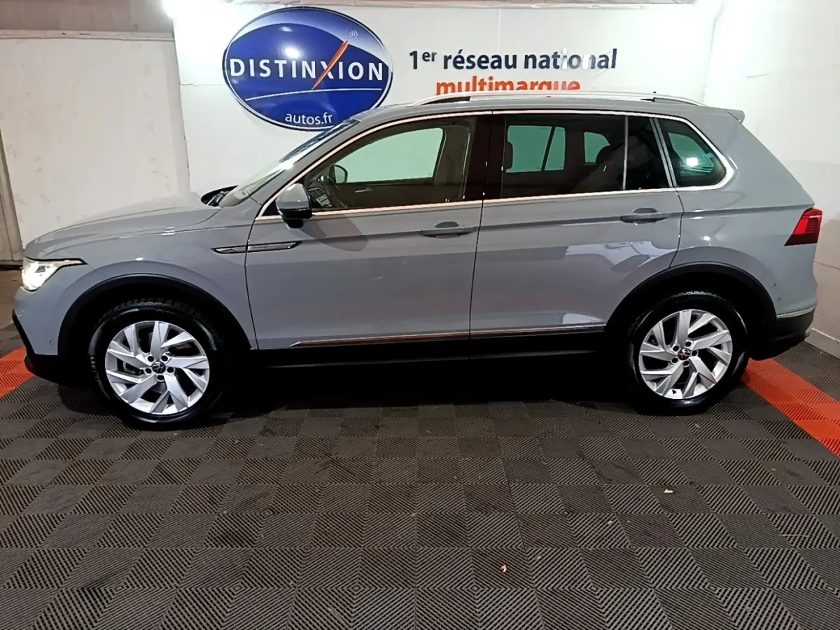 Vue latérale gauche d'un Volkswagen Tiguan gris foncé 2021 stationné en intérieur avec jantes alliage visibles.