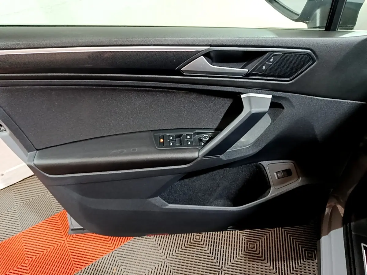 Vue intérieure de la porte côté conducteur du Volkswagen Tiguan gris foncé, avec commandes électriques et poignée argentée.