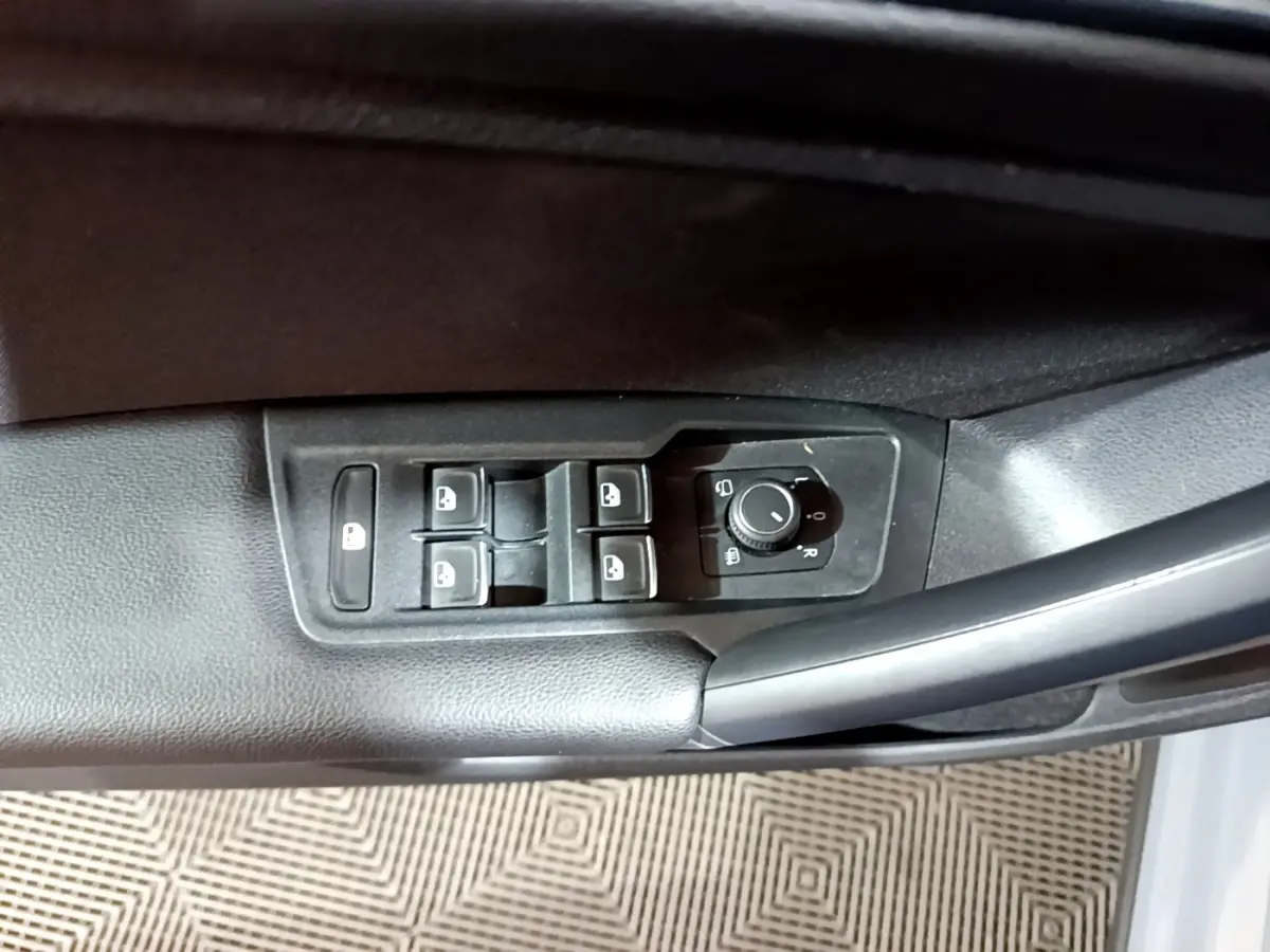 Vue rapprochée des commandes de lève-vitres et réglage des rétroviseurs sur la porte côté conducteur d'un Volkswagen Tiguan gris foncé.