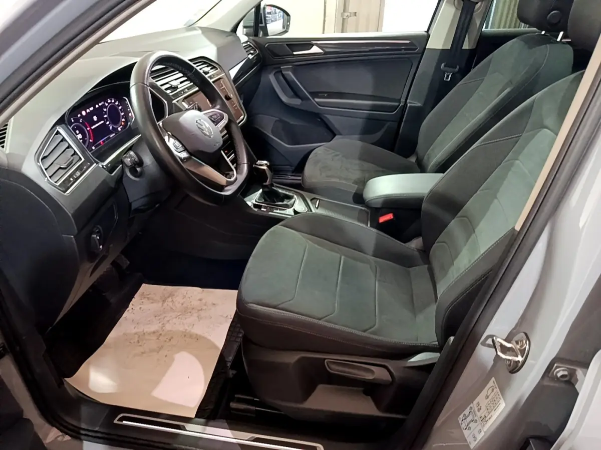 Intérieur du Volkswagen Tiguan 2021 vu côté conducteur, sièges gris foncé et tableau de bord digital lumineux.