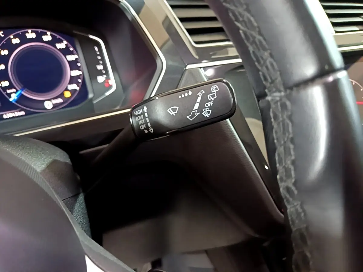 Gros plan sur la manette d'essuie-glace à gauche du volant cuir noir du Volkswagen Tiguan gris foncé, tableau de bord numérique visible.