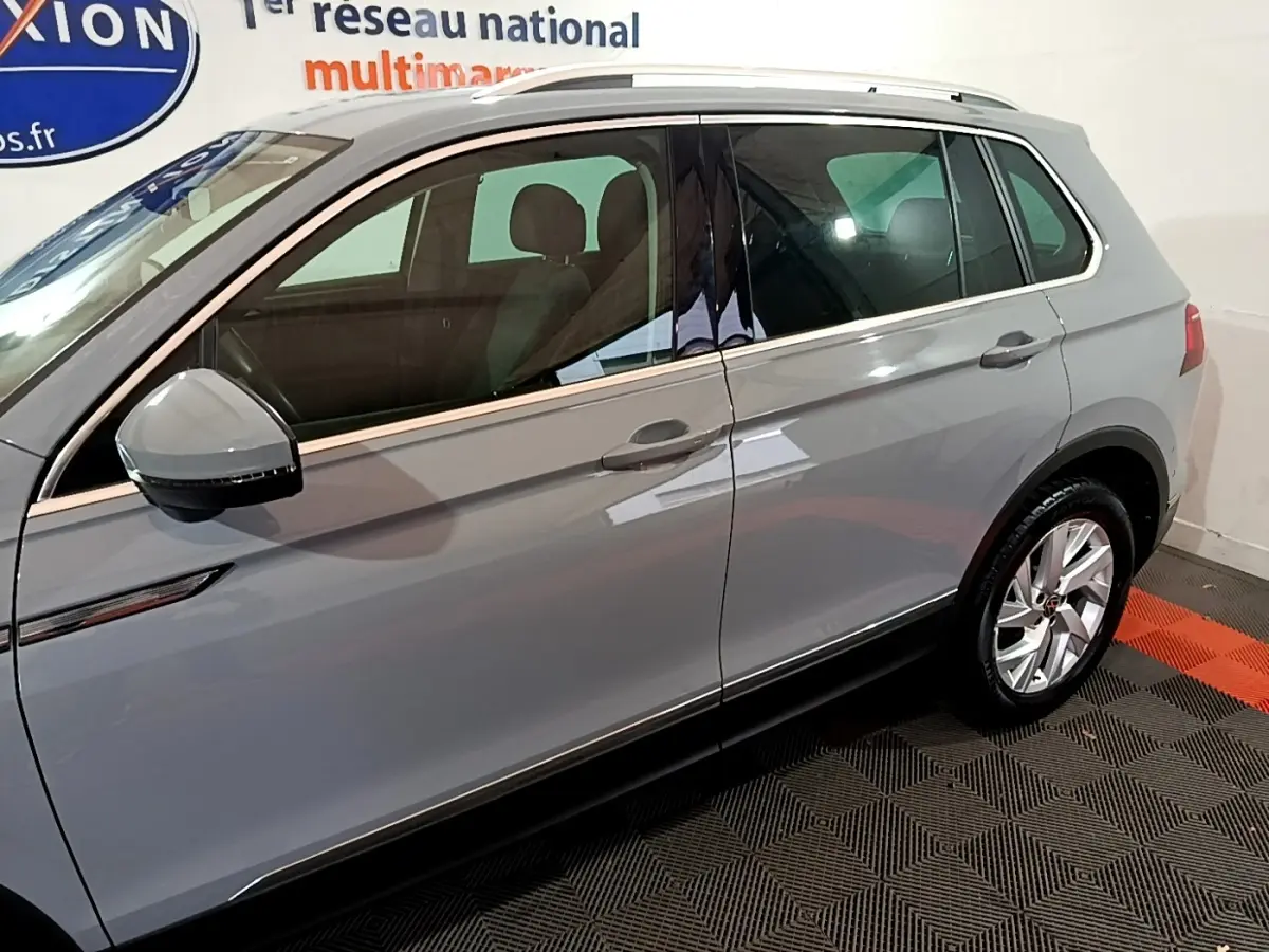 Vue latérale côté gauche d'un Volkswagen Tiguan gris foncé avec rétroviseur et jante alliage visibles.