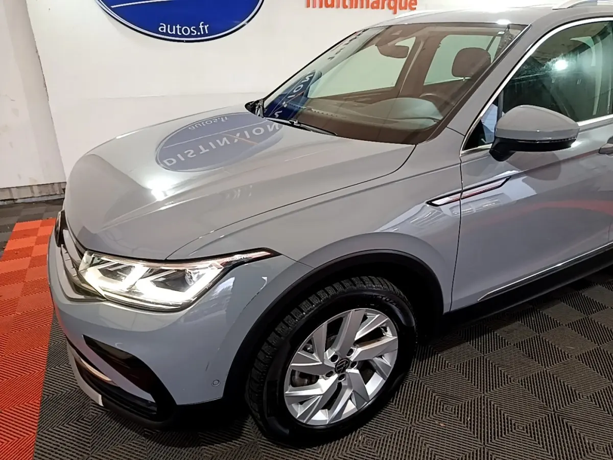 Vue 3/4 avant droit d'un Volkswagen Tiguan gris foncé avec phares LED allumés et jantes alliage visibles.