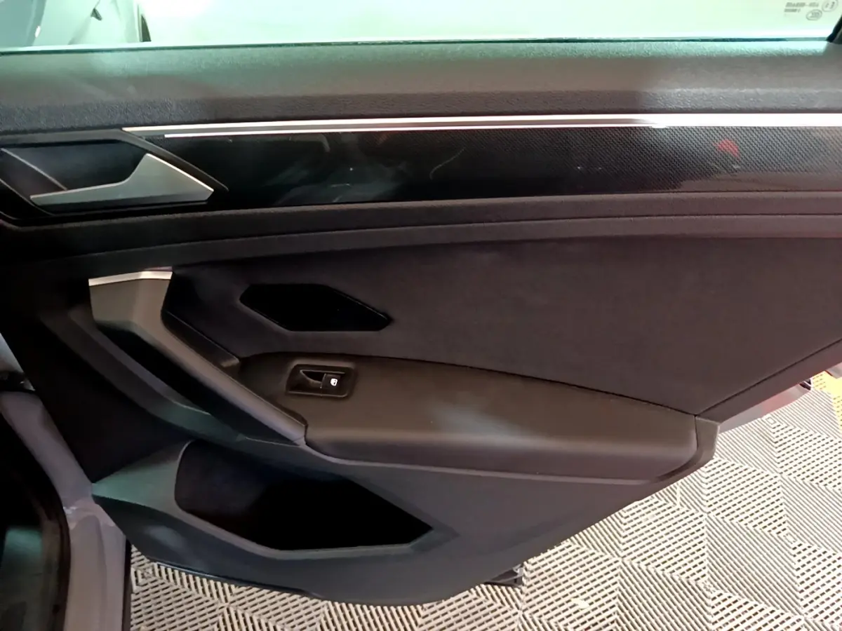 Vue intérieure de la porte côté droit du Volkswagen Tiguan gris foncé, avec poignée et bouton de verrouillage intégrés.