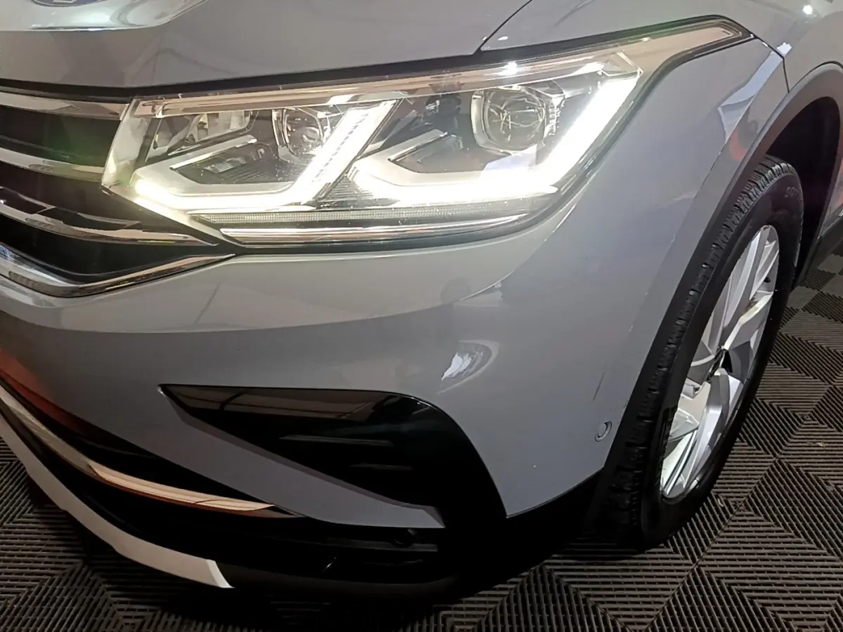 Gros plan sur l'avant droit gris foncé du Volkswagen Tiguan 2021, mettant en valeur le phare LED allumé et la roue.