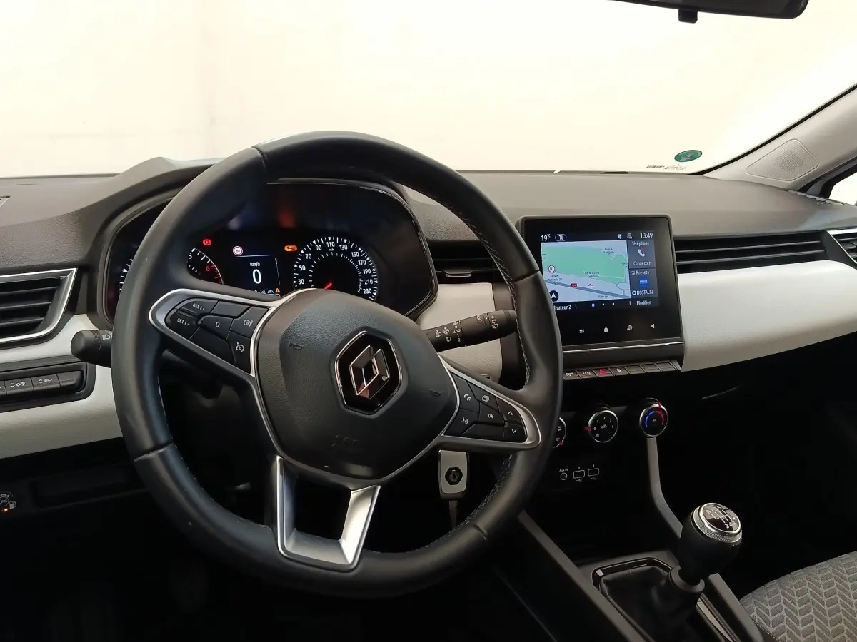 Vue intérieure de face du tableau de bord de la Renault Clio blanche, volant cuir et écran tactile central allumé.