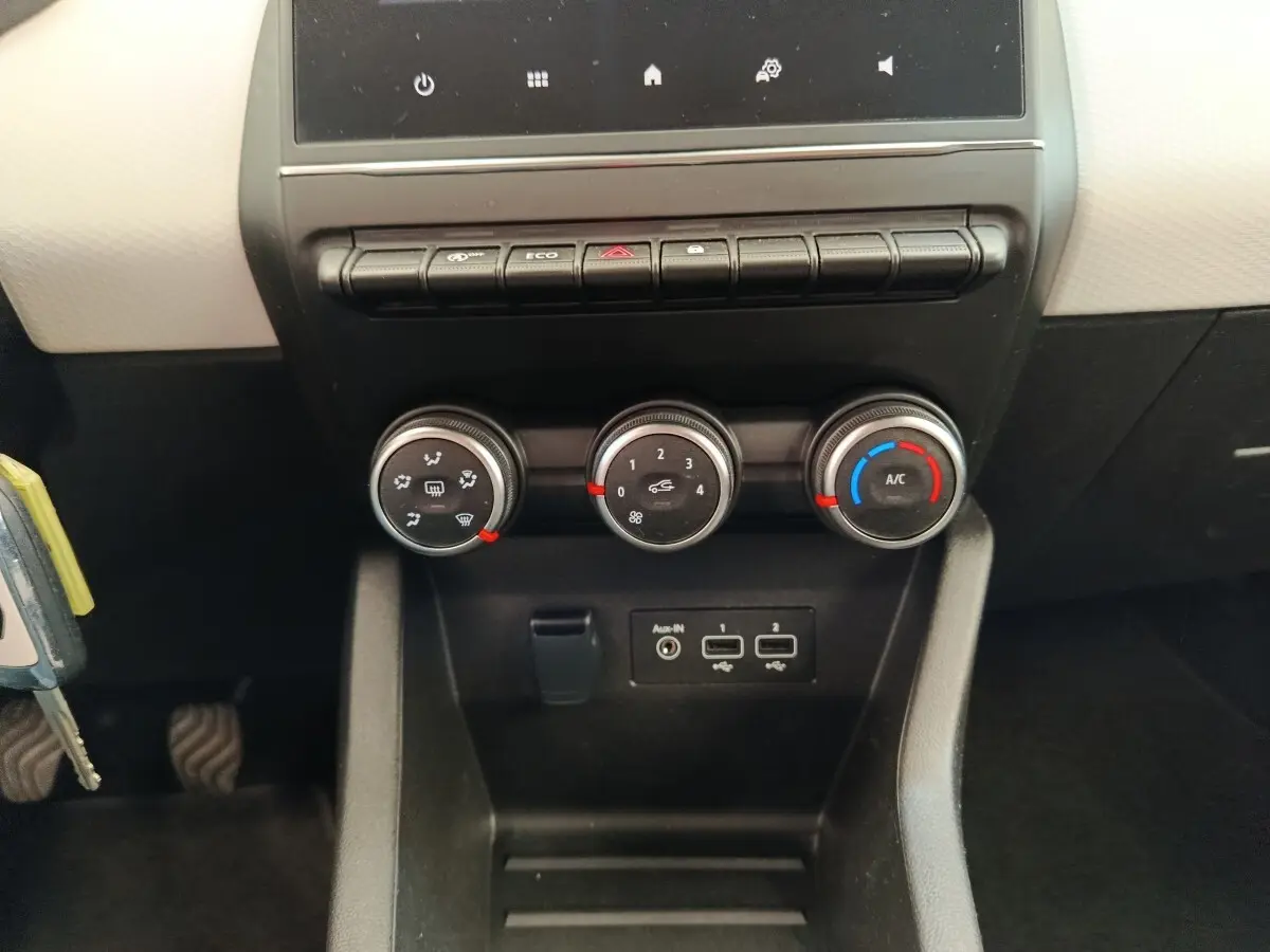 Vue rapprochée du tableau de bord central de la Renault Clio blanche 2023, avec commandes de climatisation et ports USB visibles.
