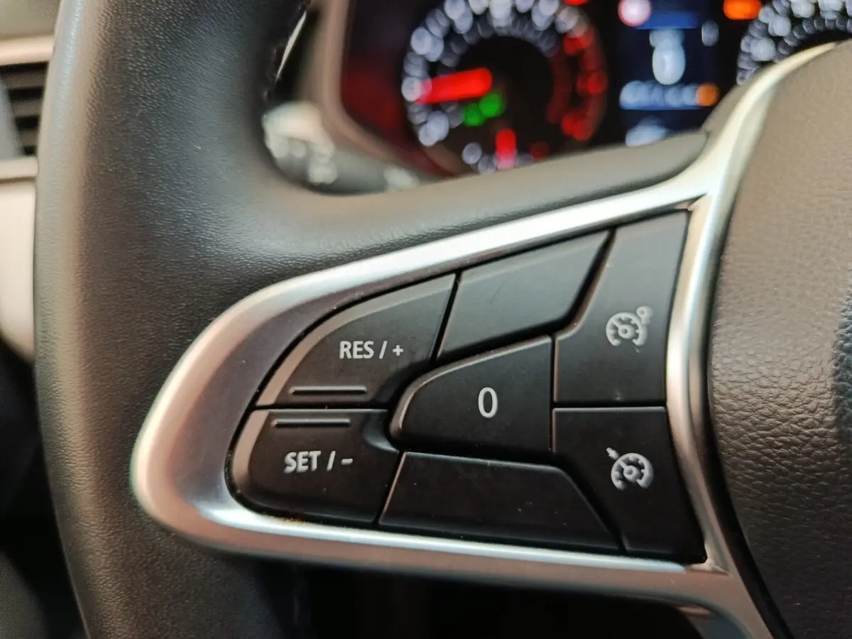 Gros plan sur les commandes du régulateur de vitesse au volant cuir synthétique d'une Renault Clio blanche 2023.