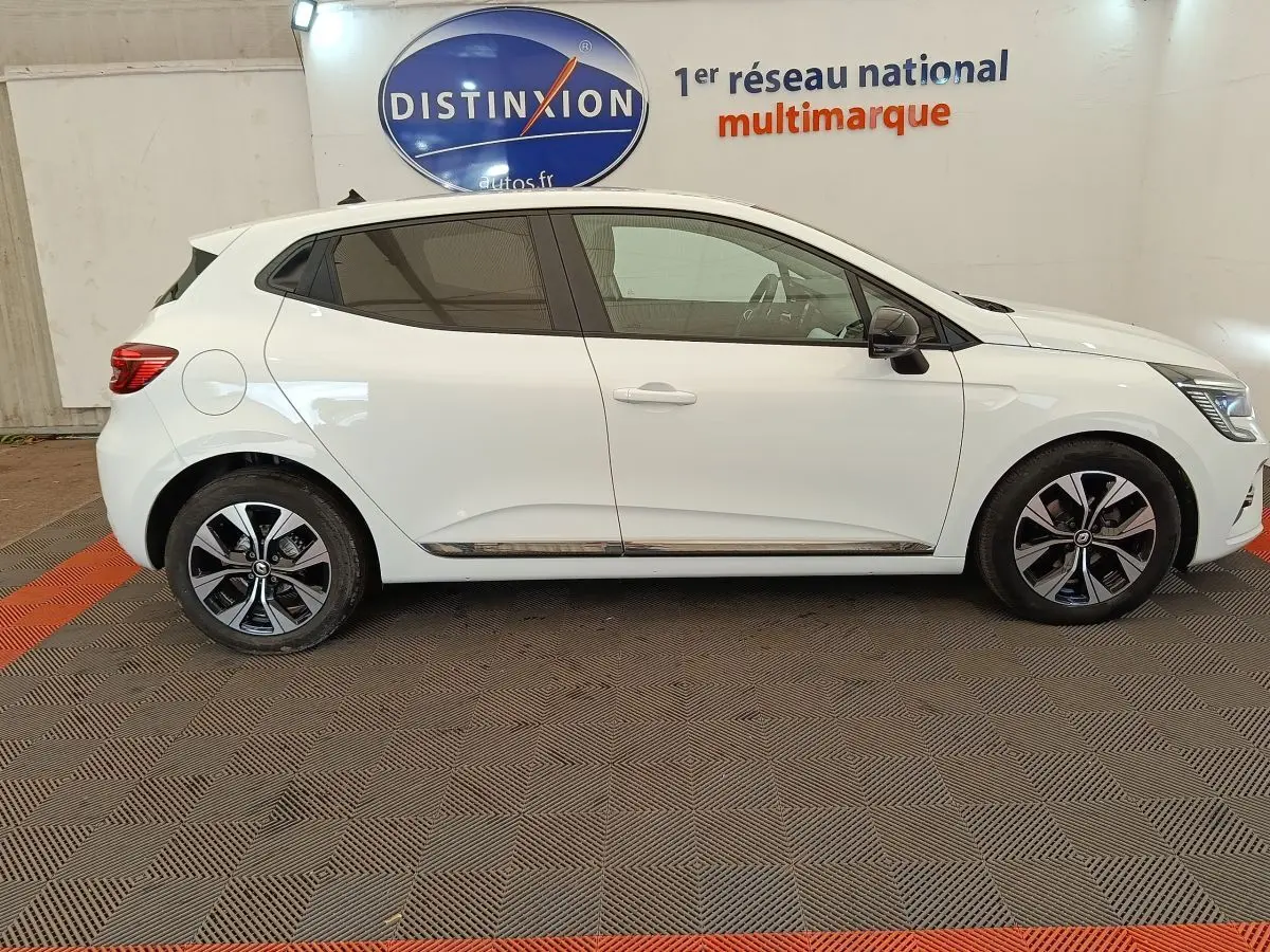 Profil droit d'une Renault Clio blanche 2023 garée en intérieur, avec jantes alliage et rétroviseurs noirs.