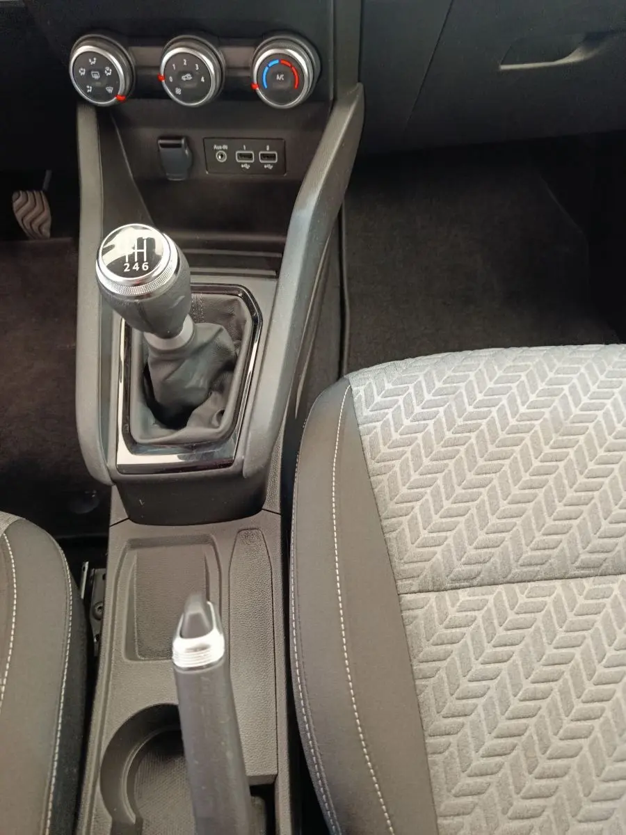 Vue plongeante sur la console centrale de la Renault Clio blanche 2023, avec levier de vitesses manuel et siège tissu gris à motifs.