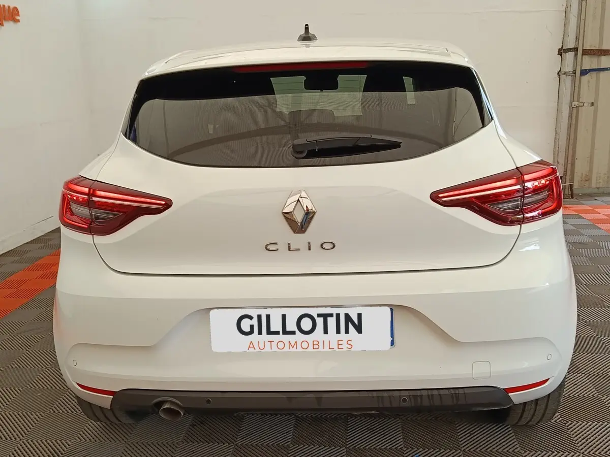 Vue arrière d'une Renault Clio blanche 2023 avec feux LED et spoiler de toit visible en intérieur.