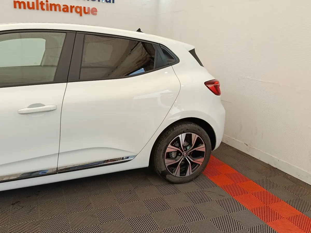 Vue latérale droite sur l'arrière d'une Renault Clio blanche avec jante alliage et baguette chromée basse.