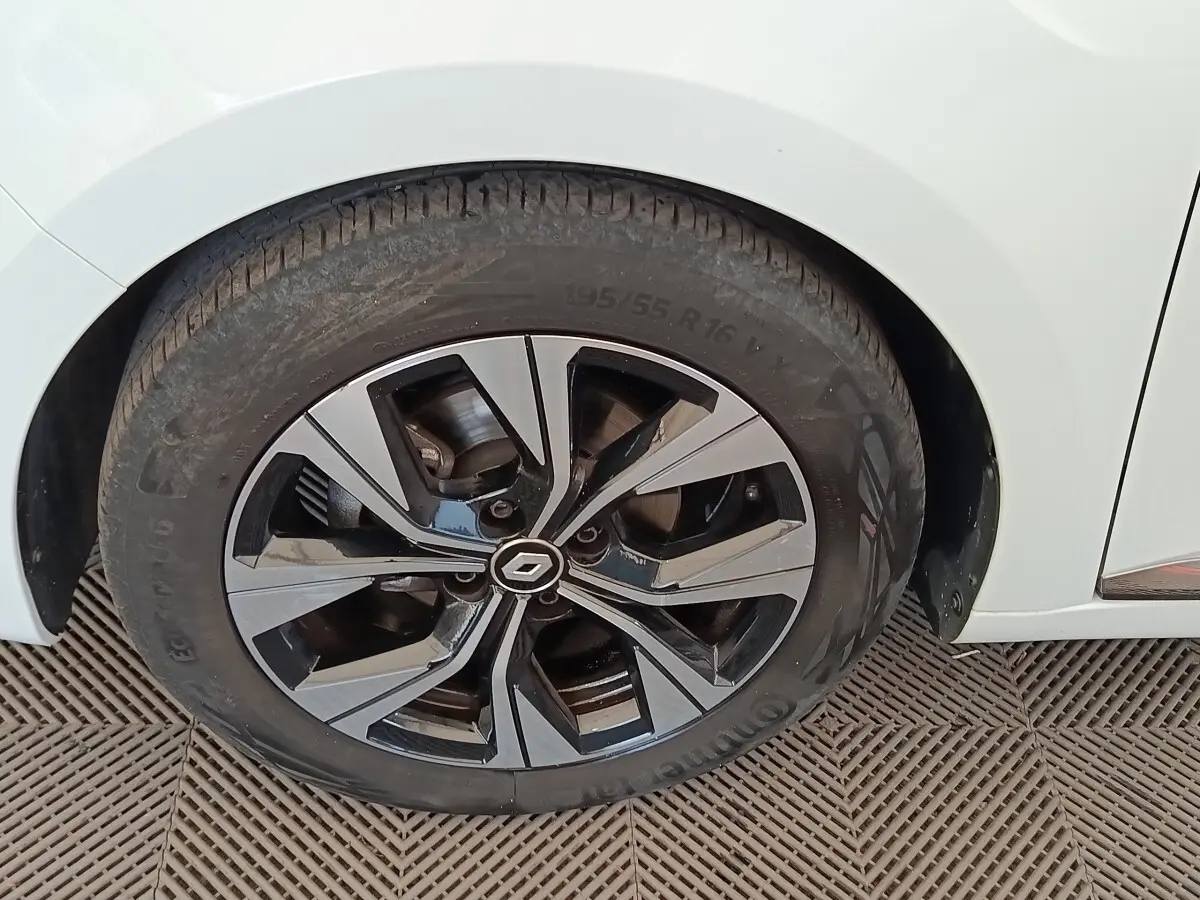 Gros plan sur la roue avant gauche d'une Renault Clio blanche, avec jante alliage bicolore et logo Renault central.