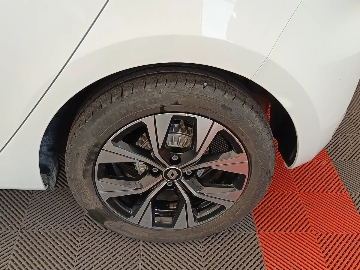 Gros plan sur la roue arrière droite d'une Renault Clio blanche, jante alliage noire au design moderne.