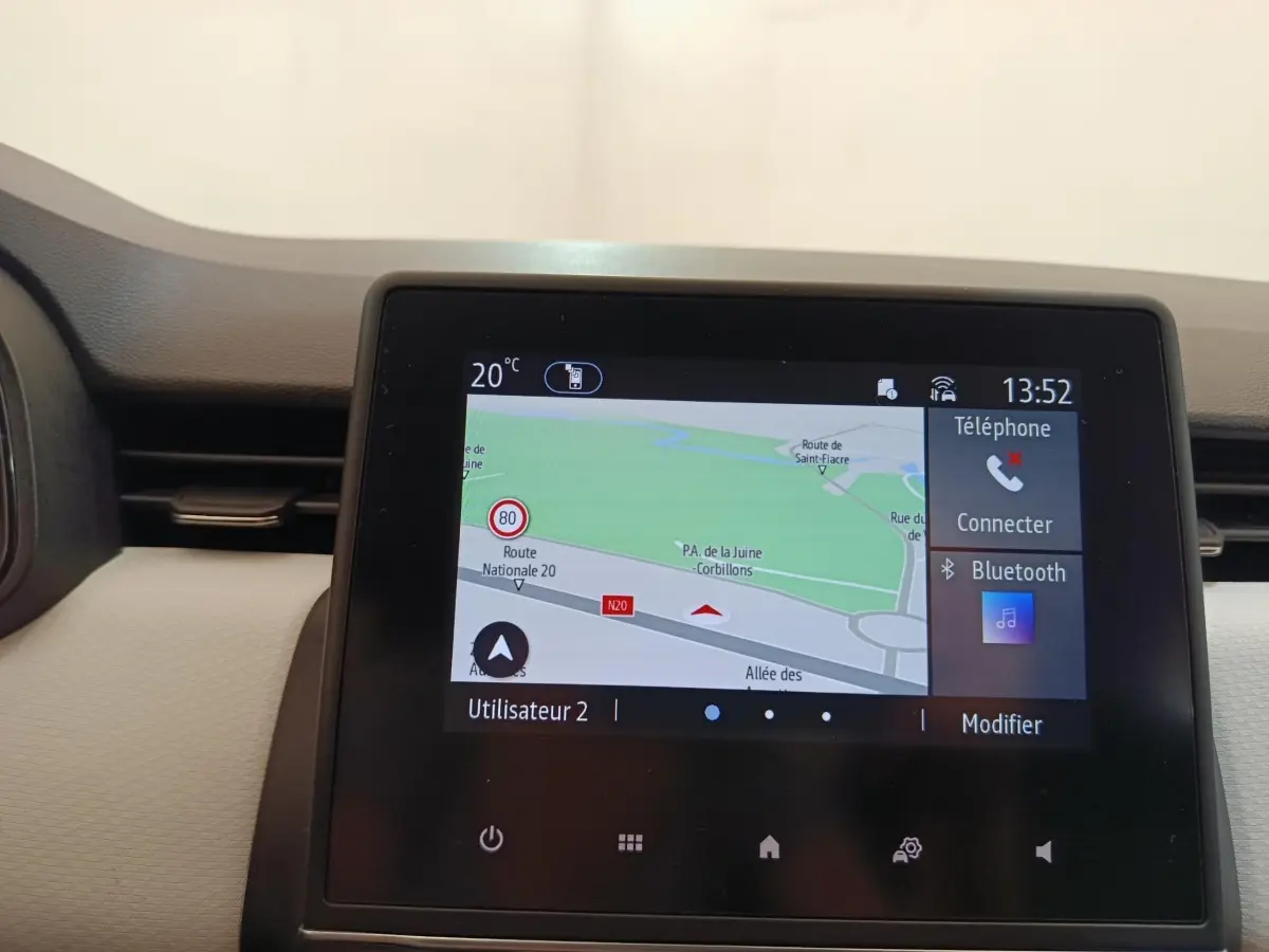 Écran tactile central de navigation 3D et Bluetooth dans une Renault Clio blanche, vue intérieure frontale.