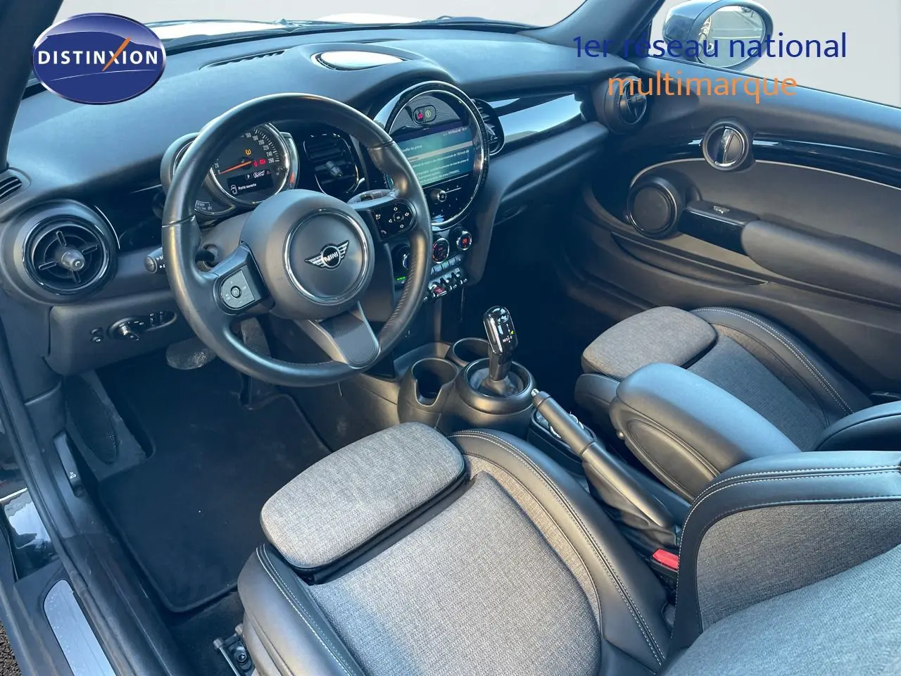 Intérieur de la MINI Cabriolet F57 2023 vu côté conducteur, sièges tissu gris et cuir noir, tableau de bord moderne avec écran central.