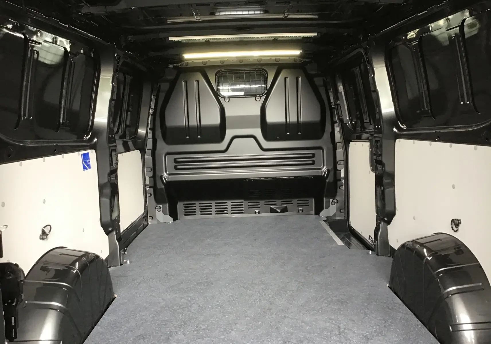 Vue intérieure arrière du Volkswagen Transporter T7 L2H1 gris anthracite, montrant l'espace de chargement avec revêtement au sol et parois renforcées.
