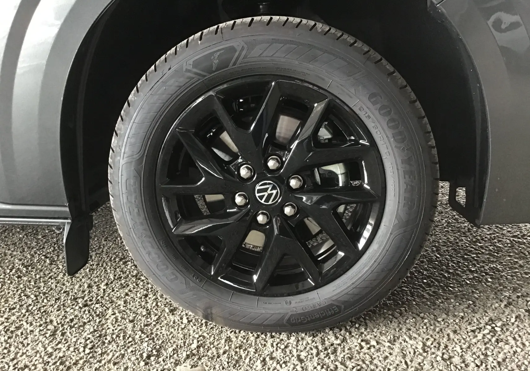 Gros plan sur la roue avant droite du Volkswagen Transporter gris anthracite, jante noire brillante avec logo VW central.