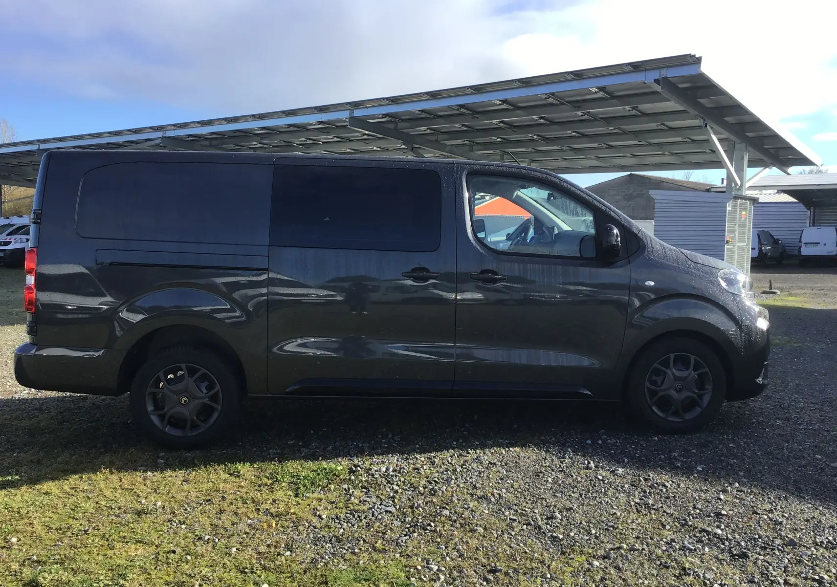 Vue de profil côté gauche d'un Citroën Jumpy Cabine Approfondie gris titane stationné sur un sol gravillonné.