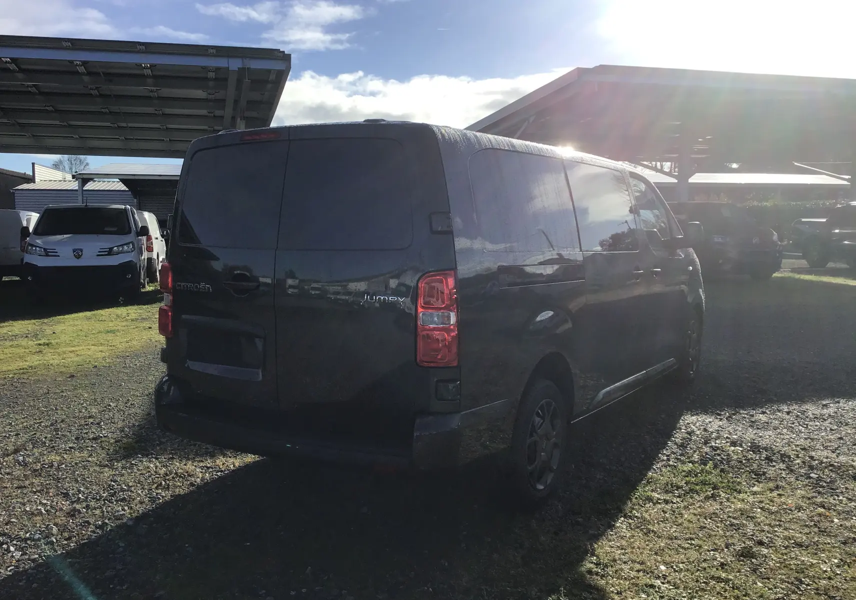 Vue 3/4 arrière droite d'un Citroën Jumpy cabine approfondie gris titane stationné sur un sol gravillonné.