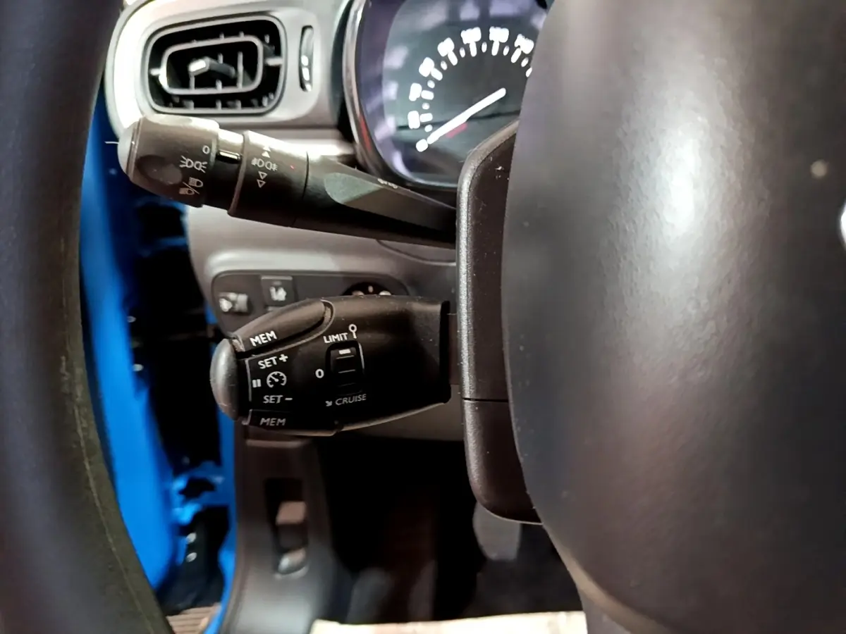 Gros plan sur la commande de régulateur de vitesse derrière le volant d'une Citroën C3 bleu 2017.