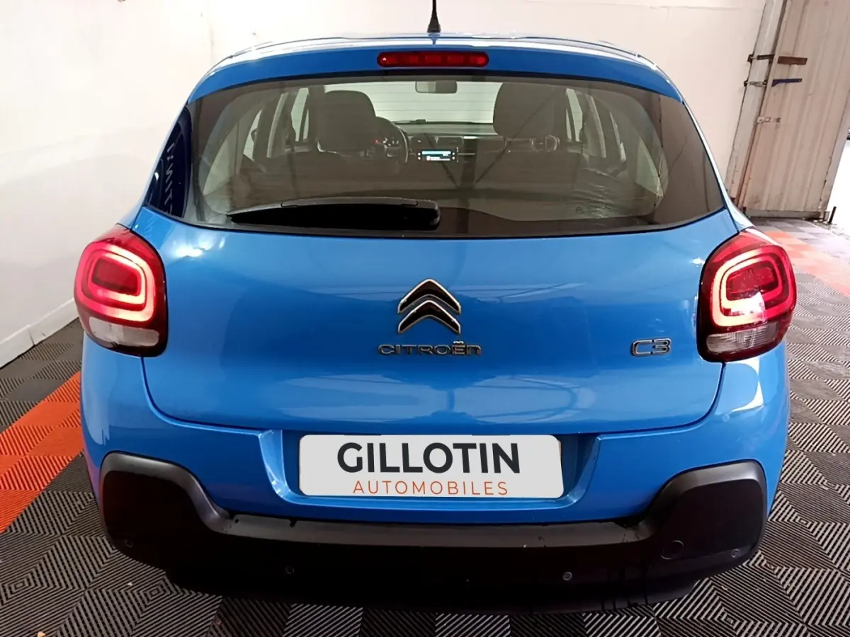 Vue arrière d'une Citroën C3 bleu vif avec feux arrière allumés dans un garage éclairé.