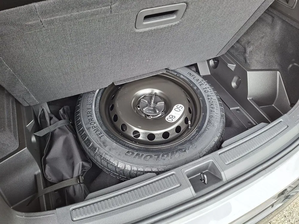 Vue du coffre ouvert du Renault Austral gris schiste, montrant la roue de secours et un sac de rangement noir.