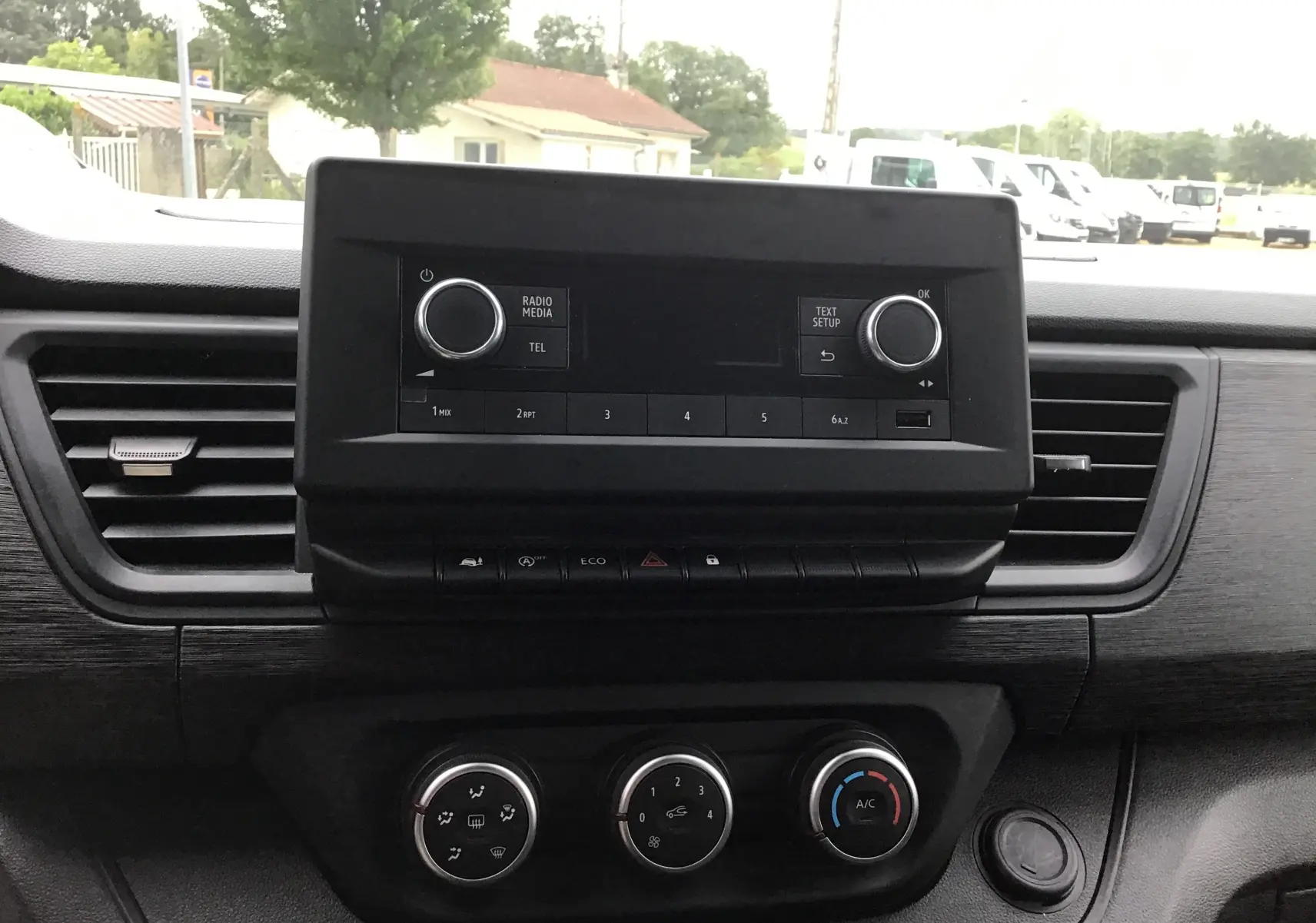 Vue intérieure centrée sur la console centrale noire du Renault Trafic Fourgon blanc, avec commandes radio et climatisation visibles.