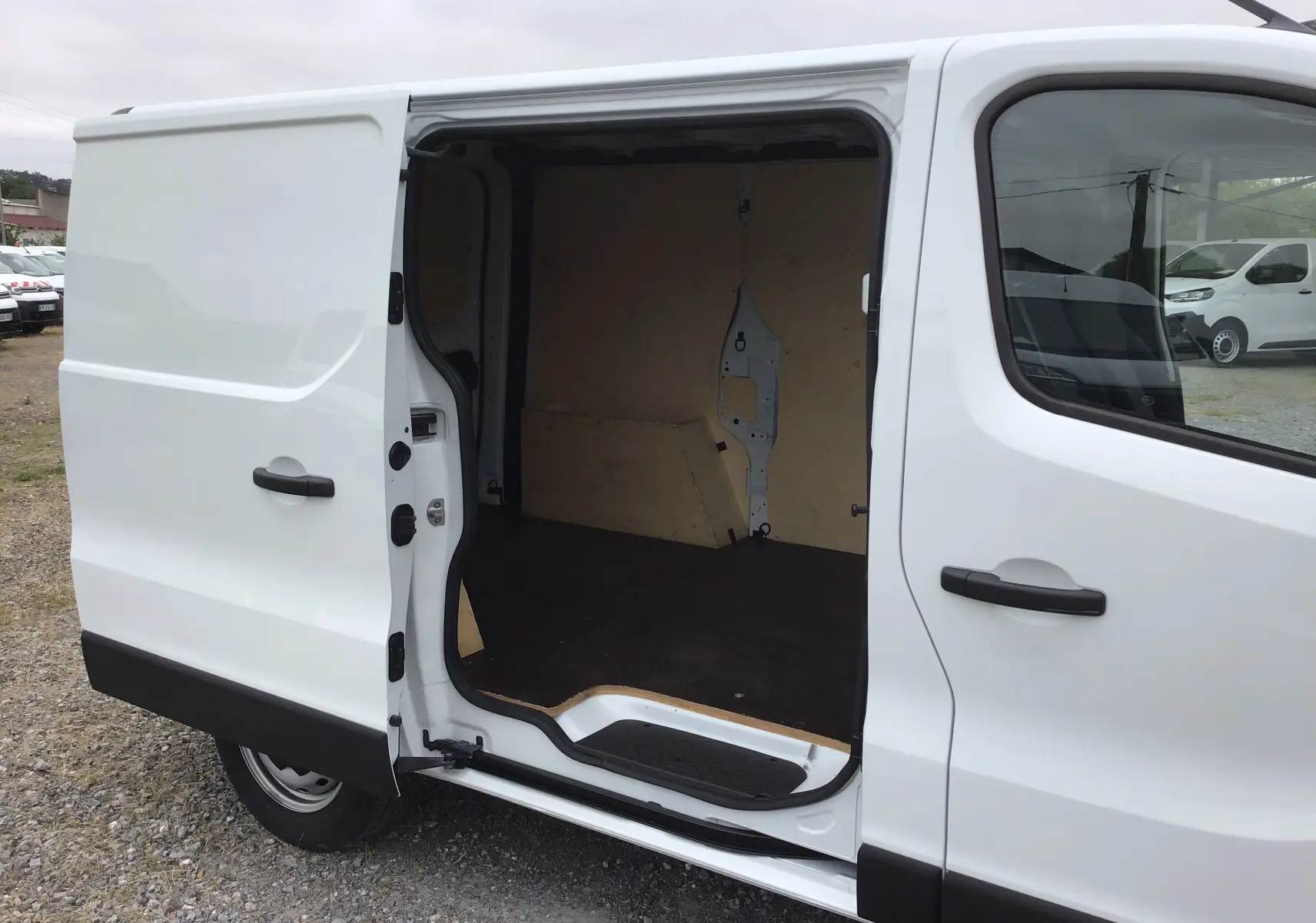 Vue latérale gauche d’un Renault Trafic Fourgon blanc 2024 avec porte coulissante ouverte montrant l’intérieur vide en bois.
