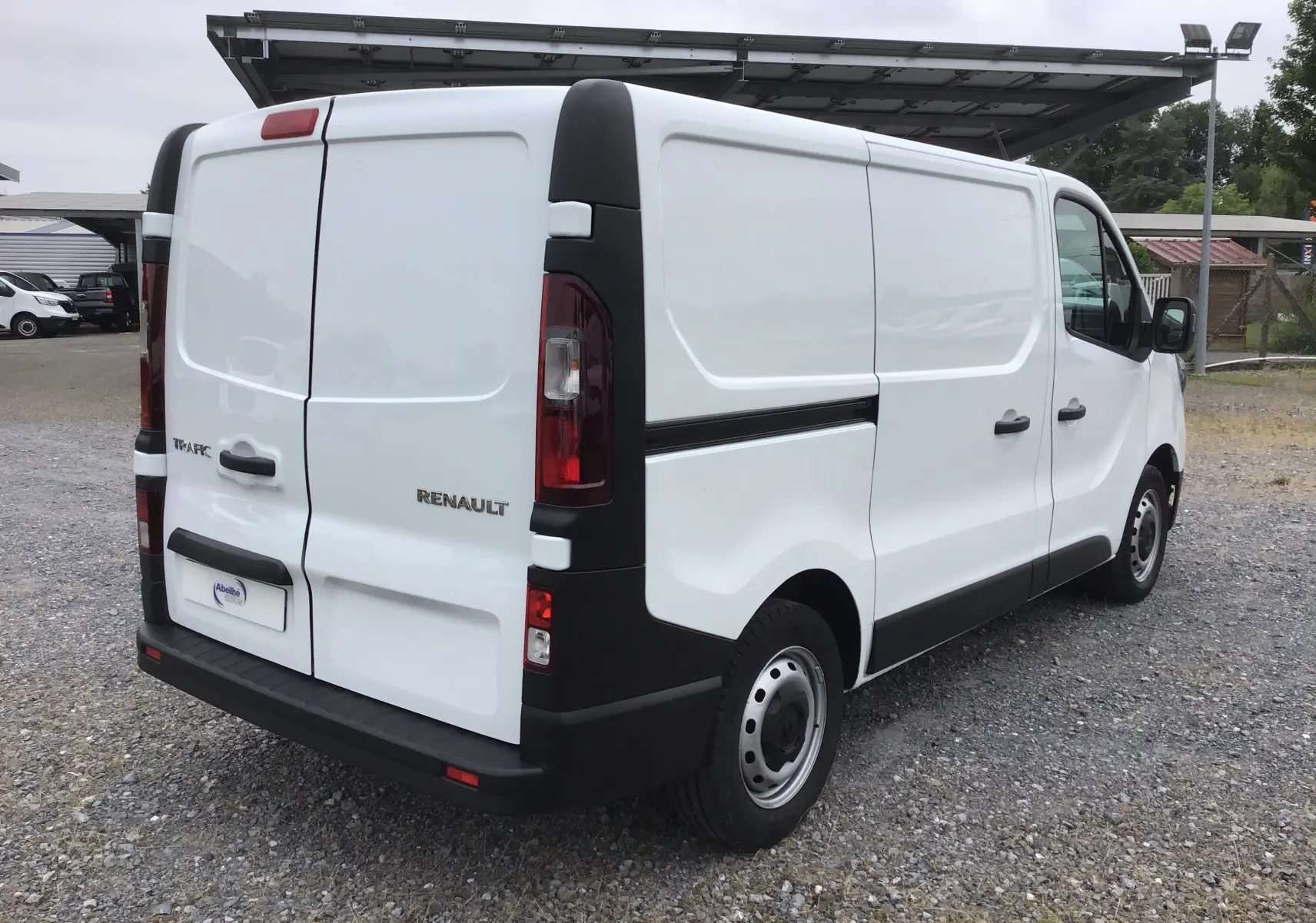 Vue 3/4 arrière droite d’un Renault Trafic Fourgon blanc 2024 avec portes arrière battantes et jantes acier noires.
