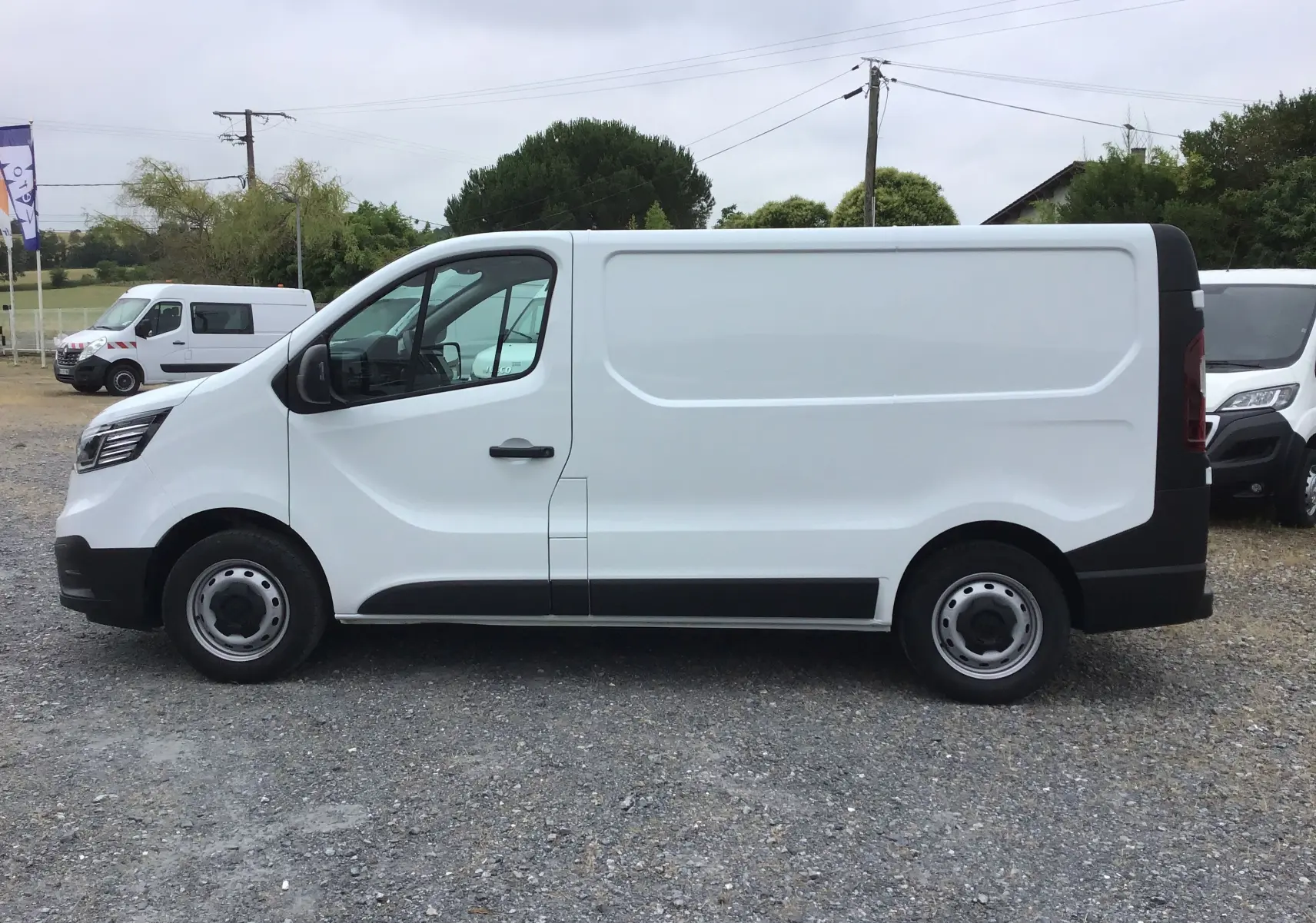 Vue de profil côté gauche d’un Renault Trafic Fourgon blanc 2024 avec protections noires sur bas de caisse et roues acier.