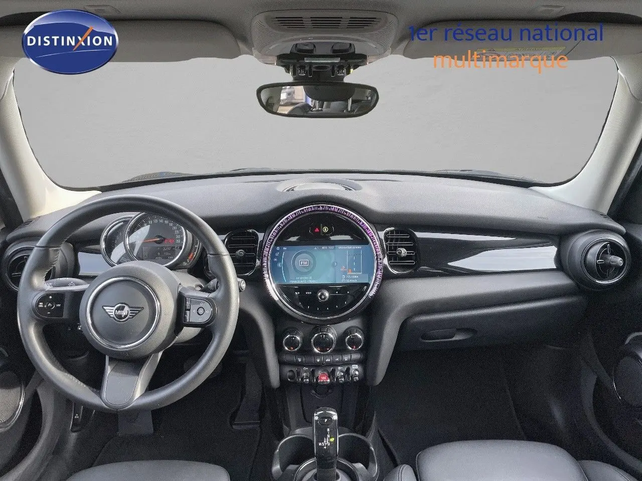 Vue frontale de l'habitacle d'une MINI 1.5 136CH noire avec tableau de bord moderne et écran central rond lumineux.