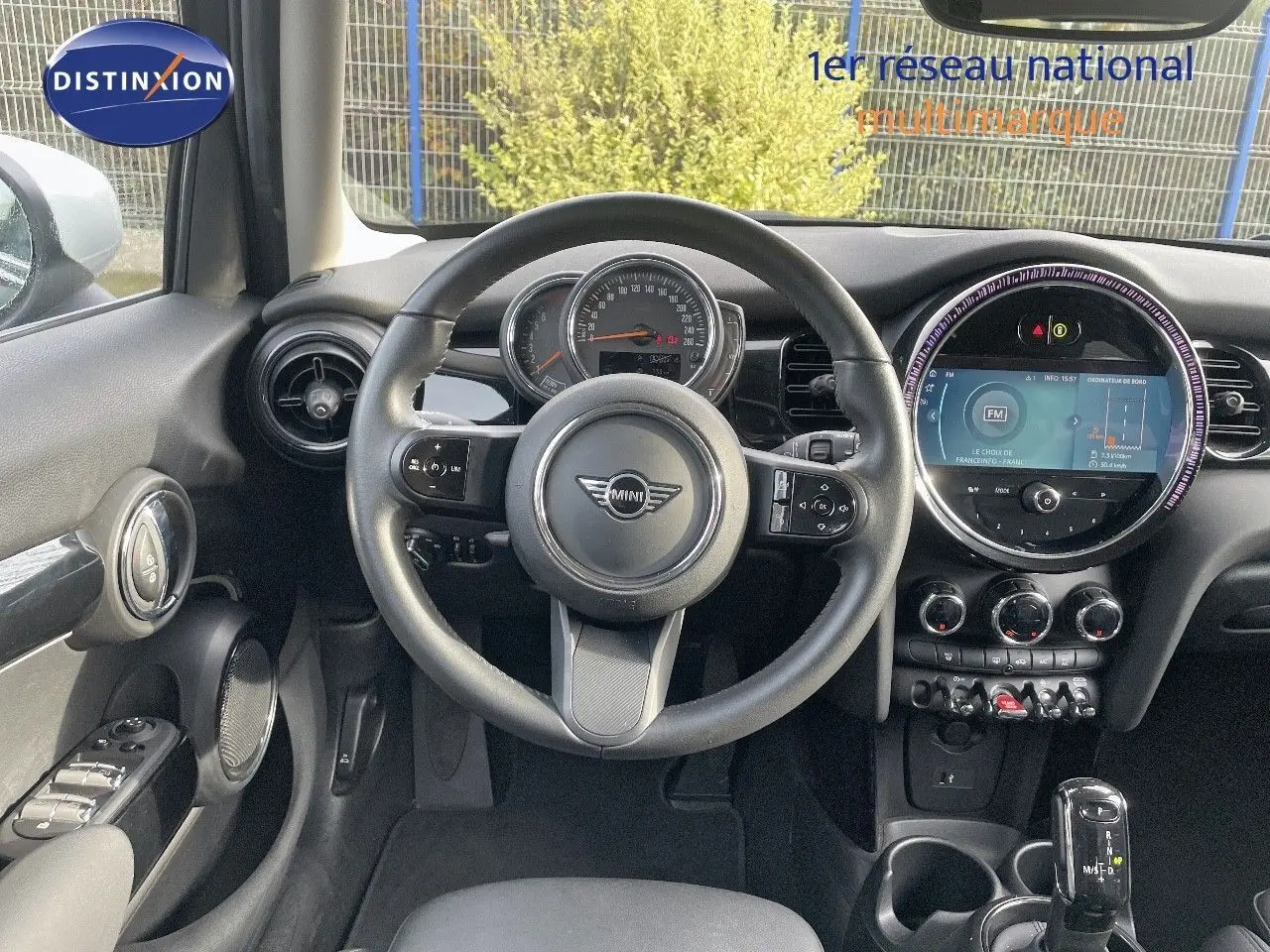 Vue intérieure avant du poste de conduite d'une MINI noire avec volant multifonctions et écran tactile circulaire.