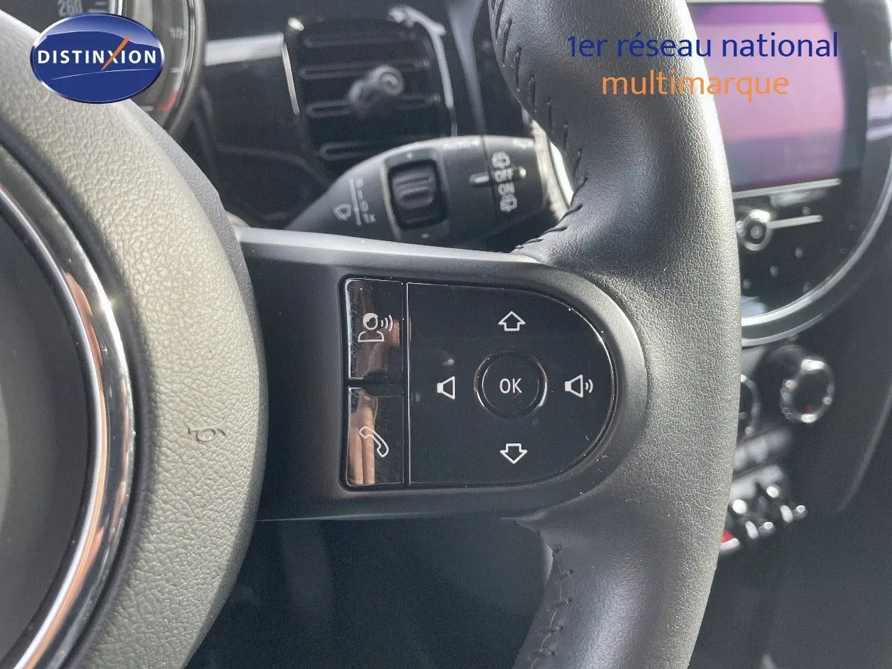 Gros plan sur le volant noir de la MINI 2023, mettant en valeur les commandes intégrées et l'écran de bord en arrière-plan.