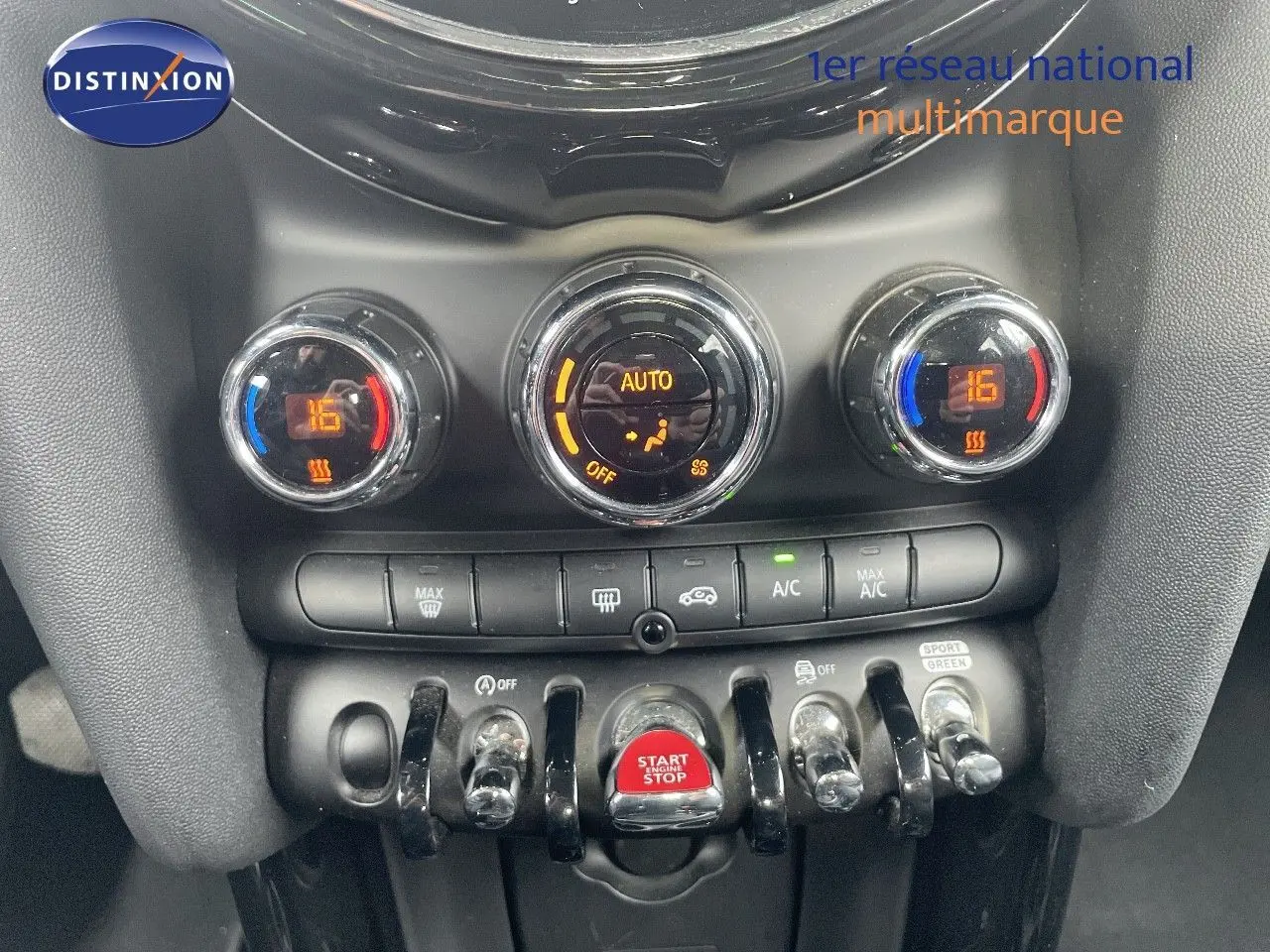 Gros plan sur la console centrale de la MINI 2023 noir midnight metal, avec commandes climatisation et bouton start/stop rouge.