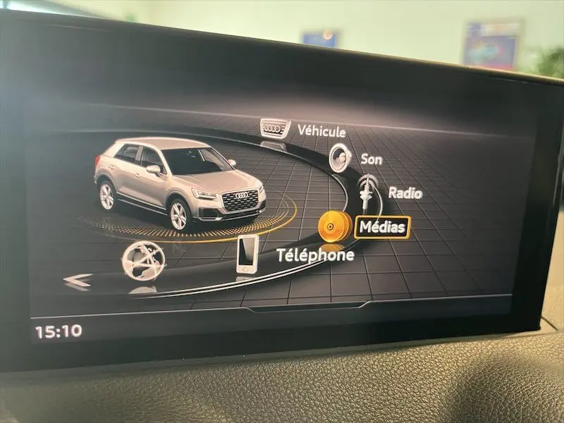 Vue 3/4 avant d'un Audi Q2 bleu Navarre métal affiché sur l'écran multimédia intérieur avec menu principal visible.