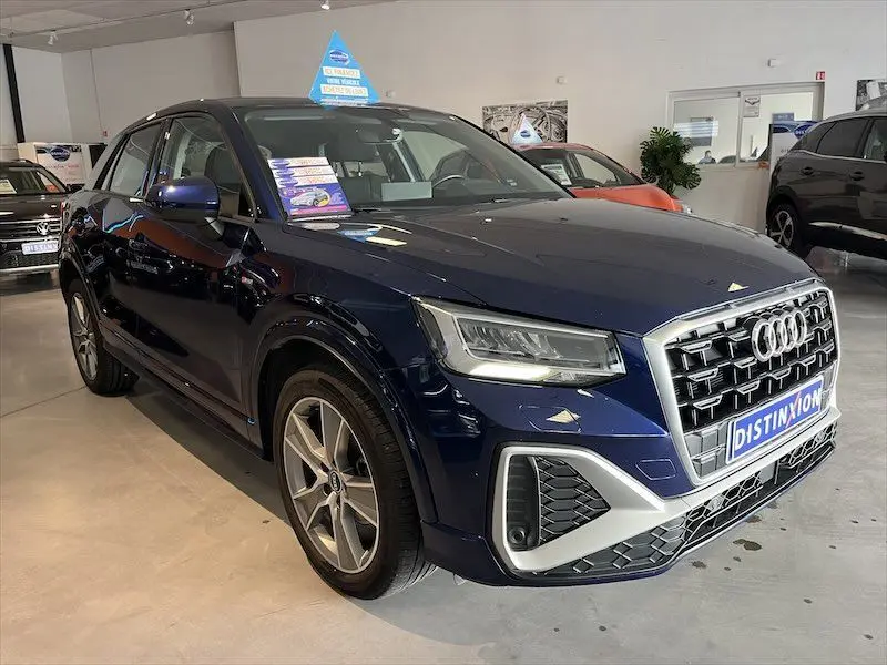 Audi Q2 30 TFSI S-Line bleu Navarre métal vu en 3/4 avant droit dans un showroom lumineux