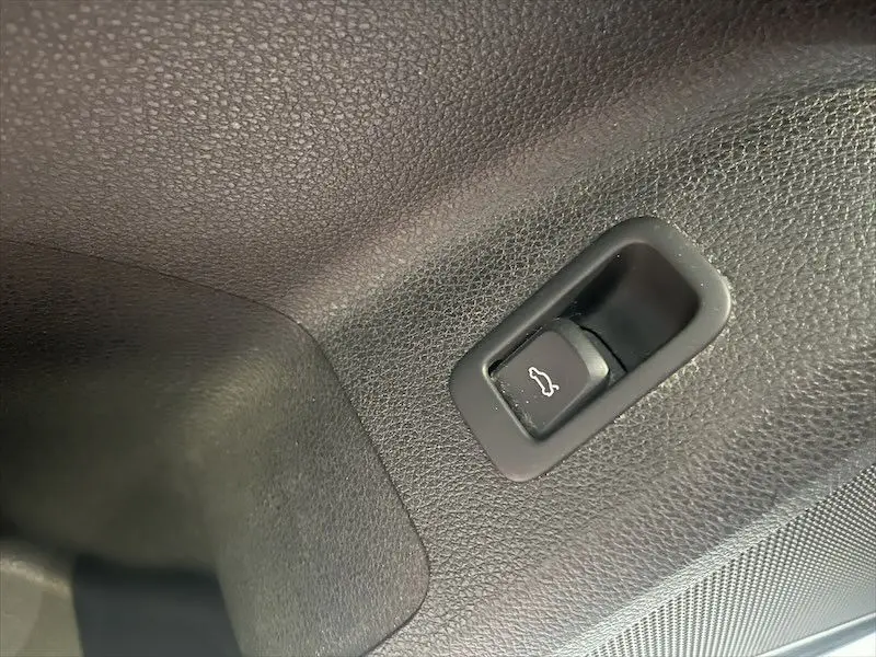 Bouton d'ouverture du coffre en plastique noir sur le revêtement intérieur texturé d'un Audi Q2 Bleu Navarre 2021 S-Line.