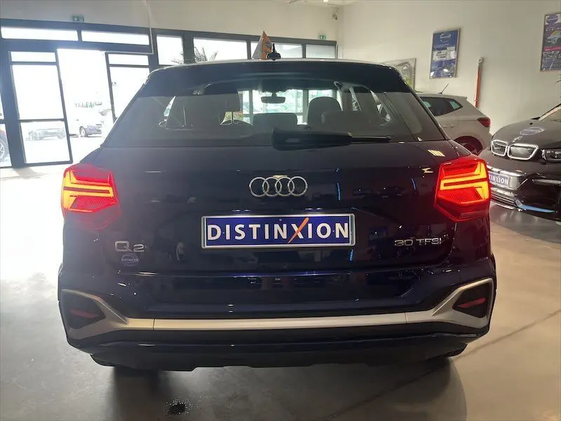 Vue arrière d'un Audi Q2 30 TFSI S-Line bleu Navarre métal avec feux allumés dans un showroom.