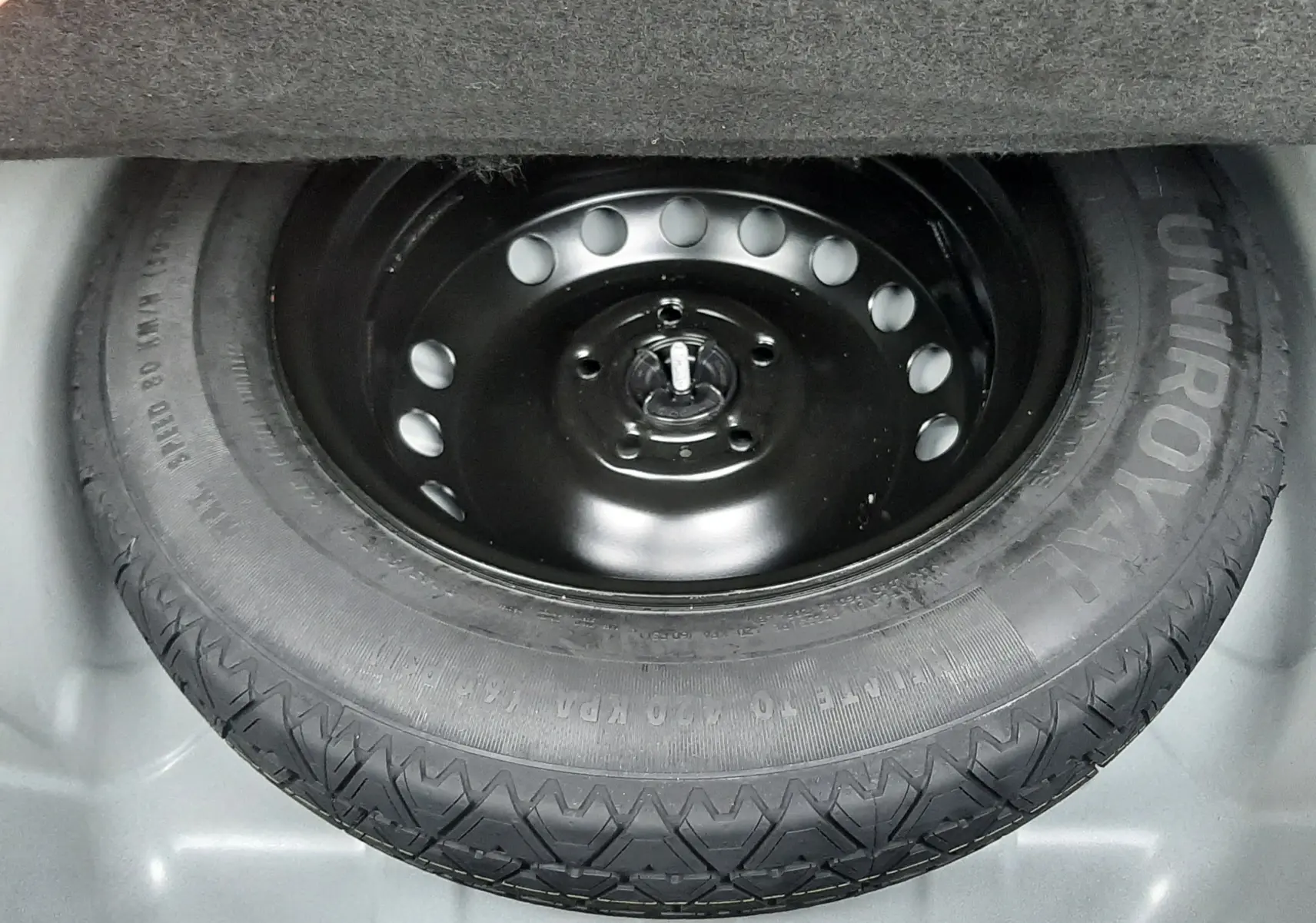 Gros plan sur la roue de secours noire Uniroyal dans le coffre d'une Renault Symbioz blanc nacré.