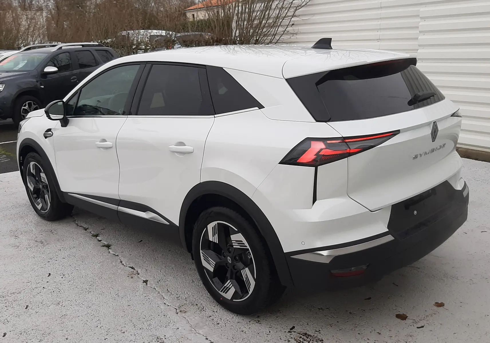 Vue 3/4 arrière droite d'un Renault Symbioz blanc nacré avec feux arrière LED et jantes bicolores modernes.