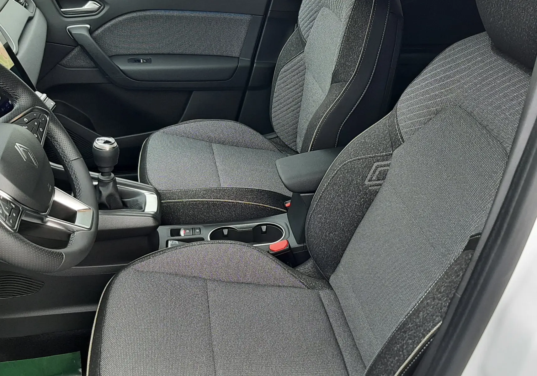 Vue intérieure côté conducteur de la Renault Symbioz blanc nacré, sièges tissu gris avec surpiqûres claires et volant multifonction.