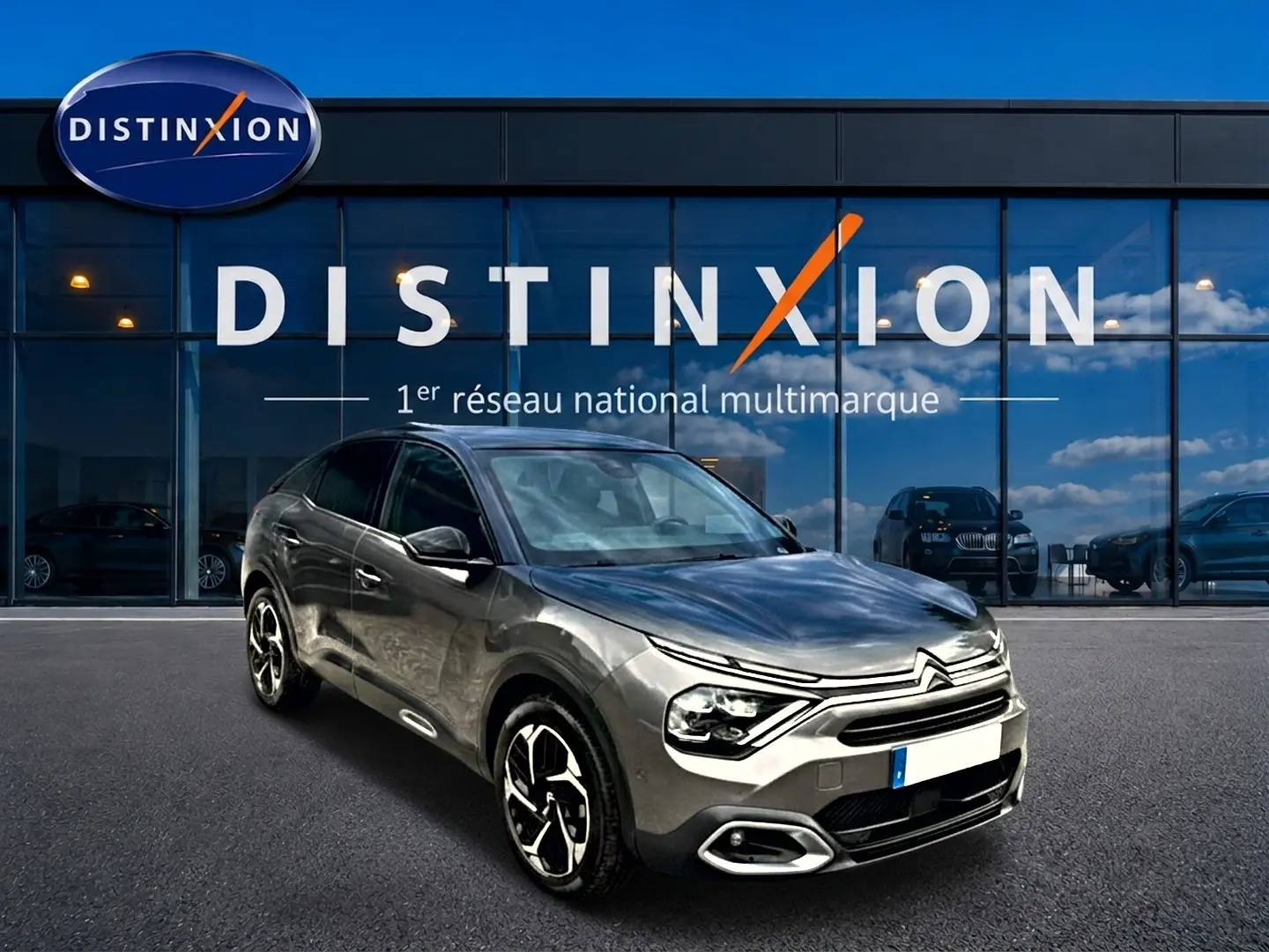 Citroën C4 gris 3/4 avant droit, avec jantes alu et calandre distinctive, devant vitrine Distinxion.