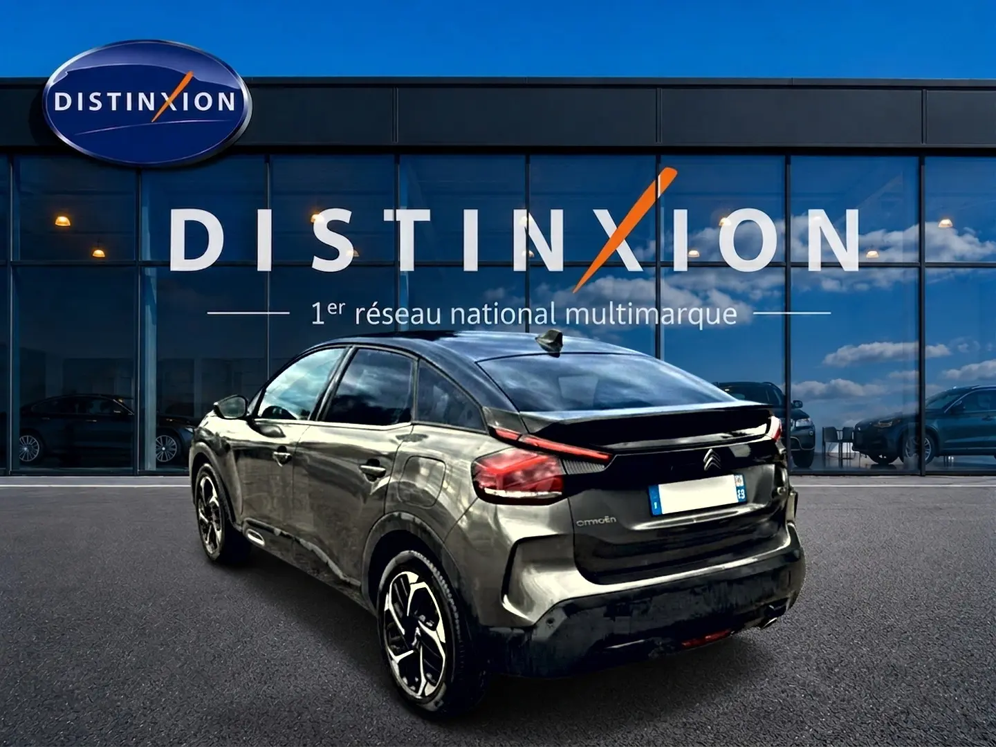 Vue 3/4 arrière droite d'une Citroën C4 gris métallisé avec jantes alliage, garée devant une vitrine Distinxion.
