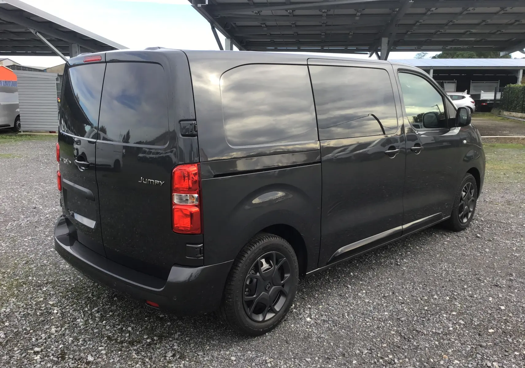 Vue 3/4 arrière droite d'un Citroën Jumpy cabine approfondie gris titane avec vitres arrière opaques et jantes noires.